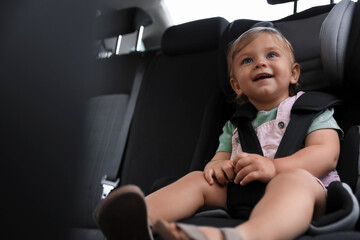 Cute little girl sitting in child safety seat inside car