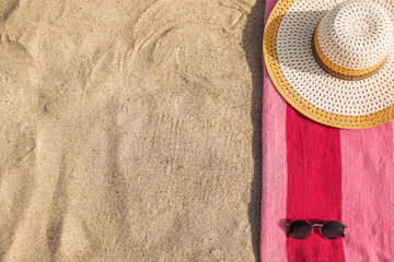 Beach towel with straw hat and sunglasses on sand, flat lay. Space for text