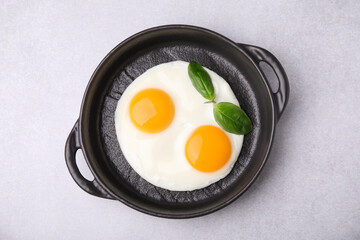 Tasty fried eggs with basil in pan on white table, top view