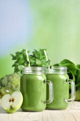 Mason jars of fresh green smoothie and ingredients on wooden table, space for text