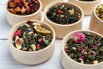 Different kinds of dry herbal tea in bowls on white wooden table