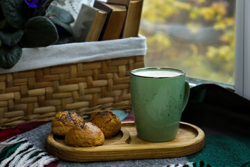 Cup of tasty hot drink and cookies near books on windowsill. Autumn coziness