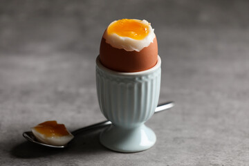Cup with fresh soft boiled egg on grey table, closeup