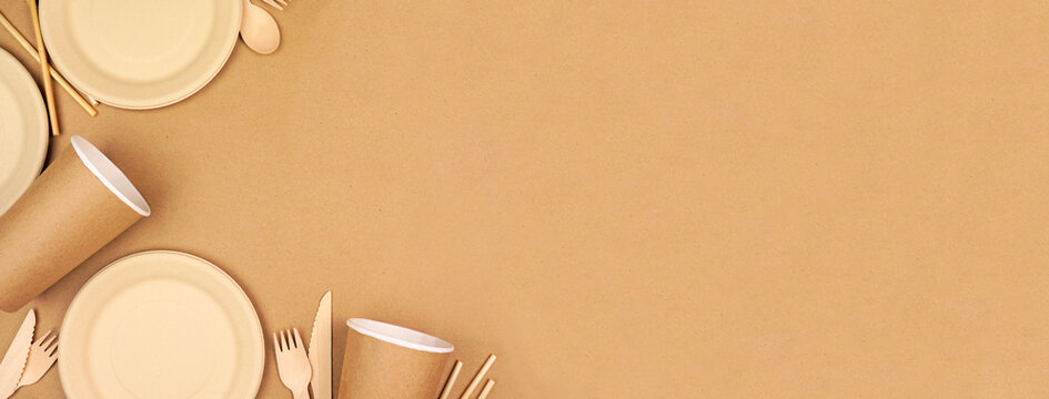 Eco friendly disposable dishware for takeout. Corner border on a brown paper background. Biodegradable, composable alternative to plastic. Top down view with copy space.