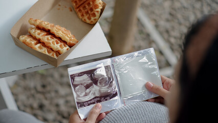 Pregnant woman holding and looking sonogram or ultrasonography picture of her unborn baby.