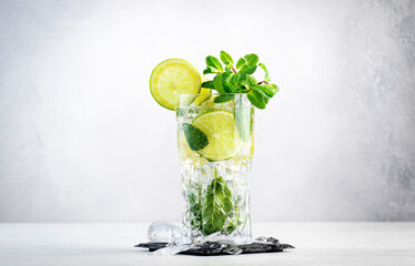Mojito classic summer alcoholic cocktail with lime, white rum, soda, cane sugar, mint, and ice in highball glass on gray background. Copy space