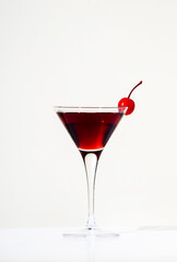 Black Manhattan cocktail with whiskey and red vermouth garnished with maraschino cocktail cherry in martini glass. Beige background, hard light