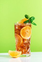 Long Island ice tea cocktail with vodka, rum, tequila, gin, liquor, lemon juice, cola and ice, garnished with lemon slice and mint in highball glass. Green background - obrazy, fototapety, plakaty