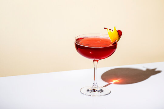 New Yorker cocktail with whiskey, grenadine, bitters, lemon juice and ice, garnished with lemon zest and cherries in glass. Beige background, hard light