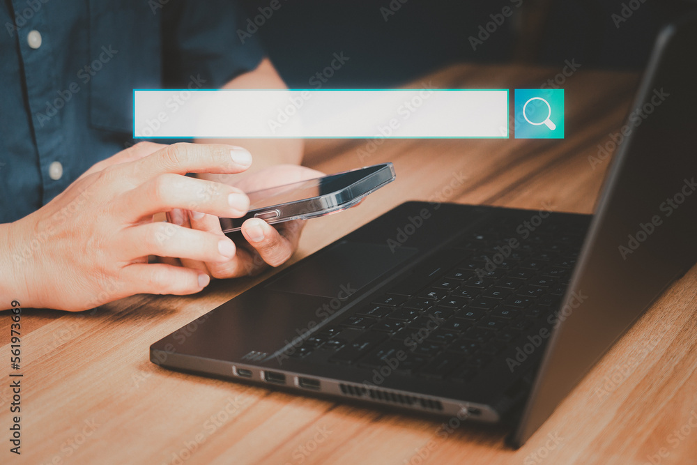 Poster Adult man hand working with a mobile phone and computer laptop on the desk. Searching browsing internet data information with blank search bar. Search Engine Optimization SEO networking concept.