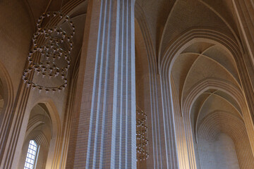 Detail of cream brick vault, arch, rib wall, column, chandelier and clerestory element on the ceiling of expressionist protestant church.