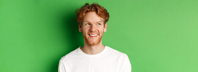 Headshot of happy redhead man with beard wearing white long sleeve, looking left at copy space and...
