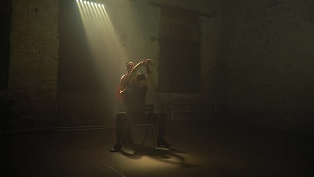 Ballroom dancers pair in abandoned old building performs passionate tango dance,man on chair,as if waking up from dream.Woman in red mini stage dress.Soft natural light source,cinema art atmosphere.
