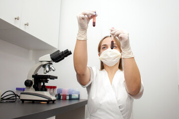 girl doctor in uniform and a medical mask holds test tubes with blood tests in the laboratory