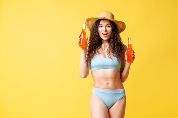 young curly brunette girl in a blue swimsuit in summer holds two bottles with an orange drink and smiles