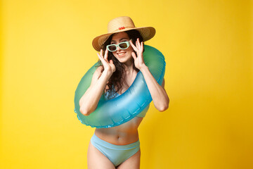 young curly brunette girl in a blue swimsuit in summer with an inflatable swim ring posing on a yellow background