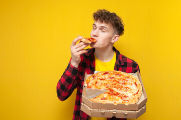 young curly guy eating pizza on yellow background, hungry student enjoy fast food