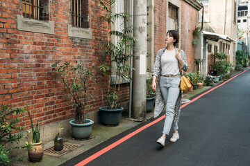 Full body of stylish positive young aged female in jeans and sneakers strolling along old Taiwan...