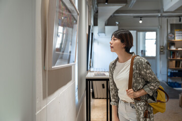 Japanese Asian woman takes look gallery collection in front framed paintings pictures on white wall with camera