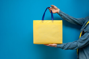 Empty yellow silk fabric tote bag with handle. Close-up of a guy holding an eco or reusable...