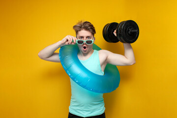 young guy in sunglasses and with an inflatable swim ring in the summer on vacation lifts a heavy...