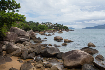 Pedras na Praia Grande - ILHABELA, SP, BRAZIL - NOVEMBER 29, 2022: Rocks on the left side of Praia Grande with houses by the sea in the background.