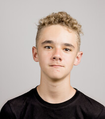 Portrait of a young boy or teenager with a funny facial expression and pimples behind a neutral background.