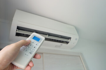 Man's hand using remote control open The air conditioner is cooled to 25 degrees Celsius in his bedroom. Health concepts and energy savings