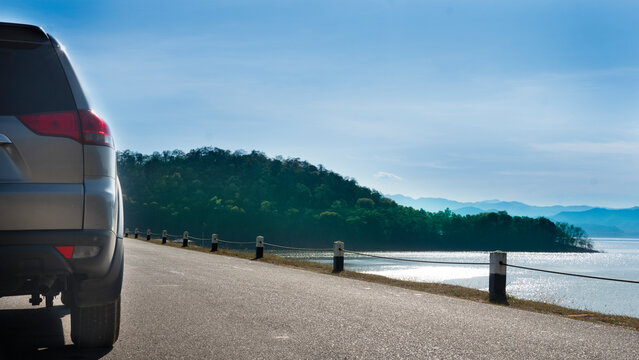 Rear side of gray car on the asphalt road. Traveling on the raod beside with water of reservoir and island under the blue sky. At Kaeng Krachan District of Phetchaburi.