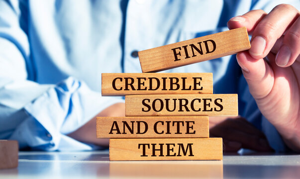 Close up on businessman holding a wooden block with "Find credible sources and cite them" message