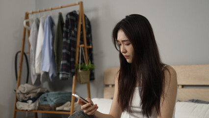 upset chinese female combing hair with hand and propping face while checking emails for her...