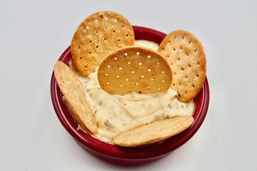 A tub of sour cream and chives dip with cracker biscuits against a white background
