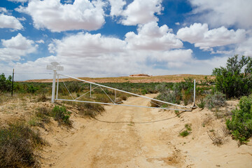Fototapeta premium White gate with 'Jesus loves you' sign in a desert in Arizona. Dry grass and sandstone formations under cloudy blue sky on hot summer day.