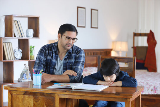 Portrait of Indian family sitting together  father advising son for studies - Education concept. Upset little child boy sitting with father in casual shirt - father explaining the importance of edu...