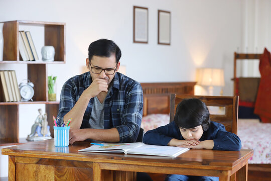 Indian father is angry and thinking about child behavior - Little child is sulking or sad  Childhood  family. Bored child boy sitting with father while doing homework wearing casual clothes  busy f...