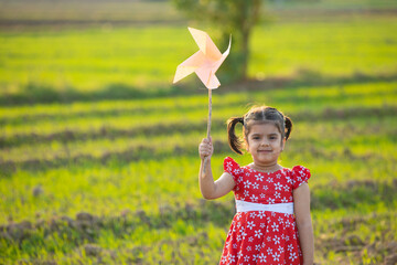 Indian little girl playing with pinwheel at agriculture field.