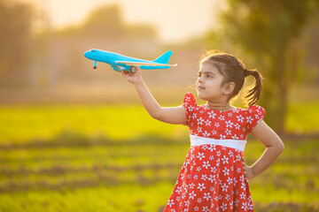 Indian little girl child playing with airplane toy at agriculture field.