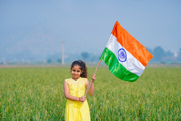 Cute indian little girl waving national tricolor flag at agriculture field.
