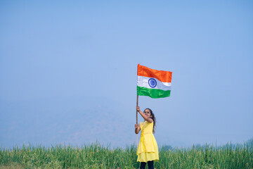 Cute indian little girl waving national tricolor flag at agriculture field.