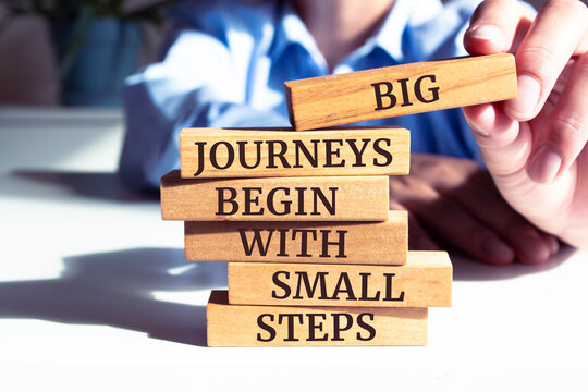 Close up on businessman holding a wooden block with "Big journeys begin with small steps" message