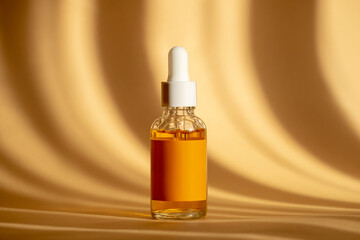 Naklejka premium Glass bottle with white dropper lid with serum on brown background in sunlight. Orange essence in transparent unmarked container. Mockup of cosmetic product for skin care