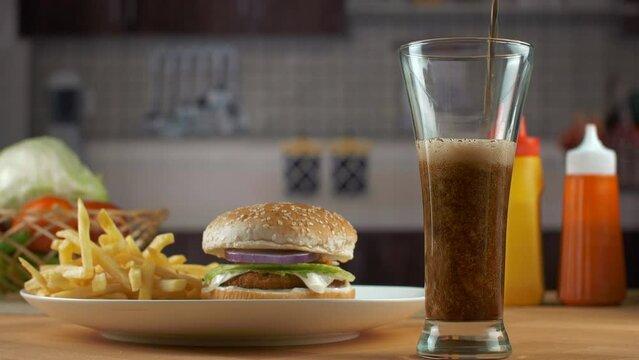 Black cola / cold drink is being poured in a transparent glass - dark fizzy drink  refreshing drink  aerated drinks. Burger is served with french fries and a glass of cold drink - snacks and refres...