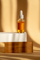 Serum is orange in transparent glass bottle with white dropper lid on wooden stand. Mockup of...