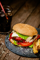 Closeup homemade beef burger with glass of soda, potatoes, tomatoes, cheese, sauce on wooden table
