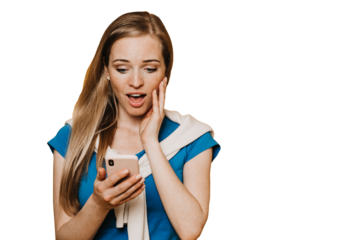 Discouraged ginger American young woman in blue t-shirt in sweatshirt tied neck holds phone looks at screen in surprise with opened mouth touches cheek excited against transparent background, message.