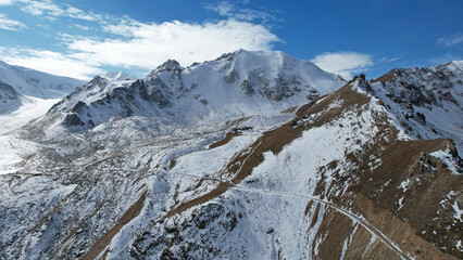 High snowy peaks and a small glaciological station. Drone view of the blue sky with clouds, steep...