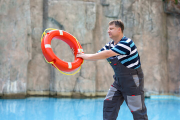 Male hotel worker throwing lifebuoy into pool.