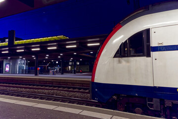 Fototapeta premium Illuminated railway station Zürich Oerlikon with platform and passengers on a dark autumn evening. Photo taken November 26th, 2022, Zurich, Switzerland.