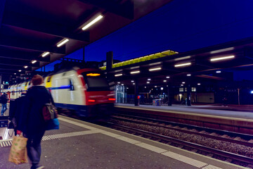Illuminated railway station Zürich Oerlikon with platform and passengers on a dark autumn evening. Photo taken November 26th, 2022, Zurich, Switzerland.