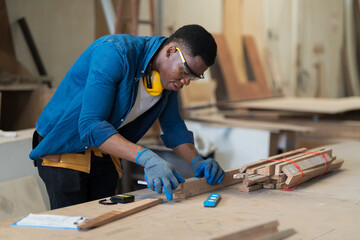 Professional African American male carpenter working in the wood workshop. Male carpenter measure...